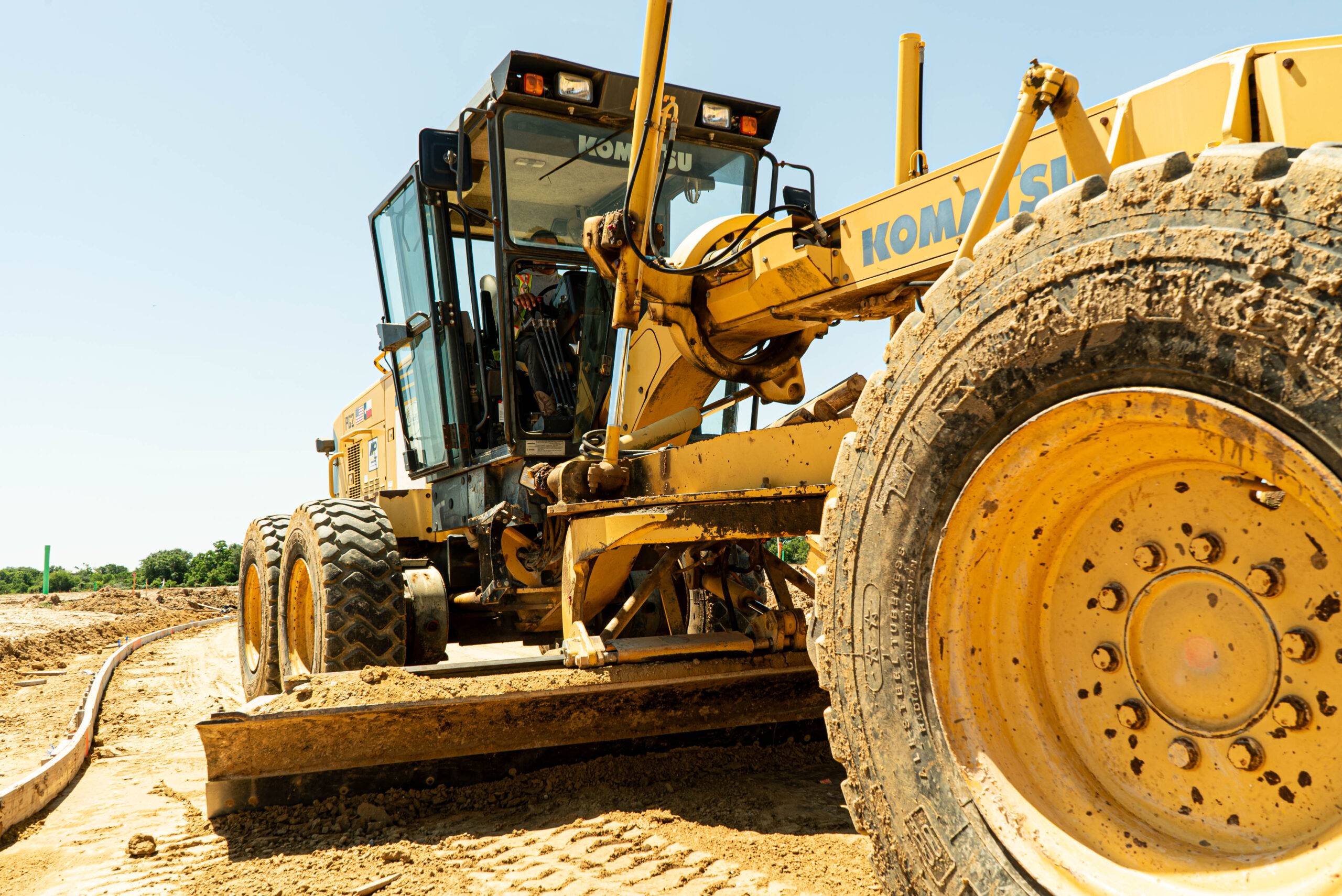 Motor grader performing roadway grading for a Texas road construction and paving infrastructure project